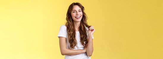 Lively joyful happy cute brunette curly long hairstyle playing curl laughing joyfully having funny amusing conversation smiling toothy white perfect smile stand yellow background relaxed photo