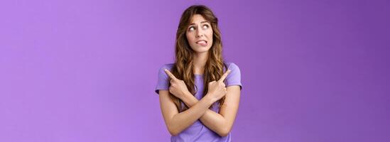 Hesitant unsure worried girl complicated make difficuly choice frowning nervously deciding look away pointing sideways cross hands chest left right anxiously choosing doubtful purple background photo