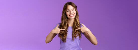 Cheerful motivated professional assertive curly woman pointing herself center smiling broadly propose own help wanna participate boastful talking accomplishments stand purple background photo