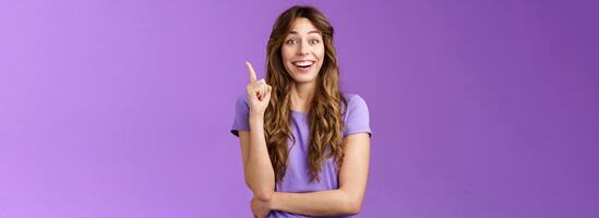 Got excellent idea. Attractive cheerful curly-haired female raise index finger eureka gesture smiling broadly made decision think up good plan share thought grinning ambushed purple background photo