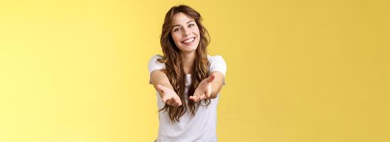 Come closer take my hand. Cheerful lovely charismatic tender woman extend arms forward camera wanna hold receive charming gift tilt head smiling pleased grateful stand yellow background photo