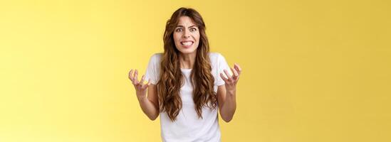 Annoyed curly-haired caucasian irritated distressed girl cringe outraged clench teeth frowning furious sqeez fists hateful complaining arguing pressured upset fighting have quarrel yellow background photo