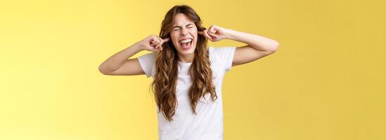 Girl yelling annoyed demand stop playing guitar. Bothered irritated woman close eyes screaming disappointed plug index fingers ear holes disgusted loud terrible noise music stand yellow background photo