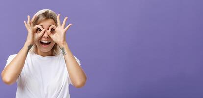 Looking at awesome discounts. Portrait of impressed amused and happy good-looking stylish young woman with tattoos on arms making circles with hands over eyes smiling with admiration at camera photo