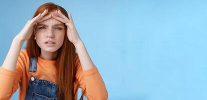 Puzzled unsure cute funny redhead european woman searching someone squinting cannot see without glasses peer into distance hold hands forehead cover sight sunlight, standing blue background photo