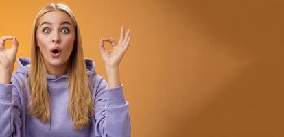 Amused talented creative young blond female tell excellent idea show okay no problem gesture persuade friends everything alright standing excited orange background ok signs, folding lips amazed photo