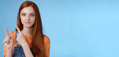 Assertive good-looking redhead girl know what talking about pointing upper left corner index fingers showing confidently good product recommend check out standing blue background photo