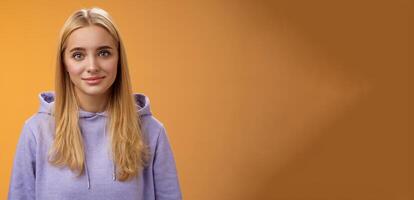 Waist-up delicate tender friendly-looking blond european girl in hoodie smiling supportive talking listening friends story nice interesting conversation standing casually orange background photo