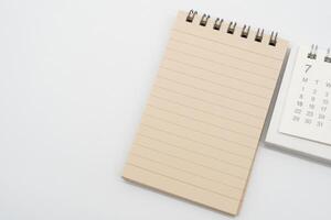 Empty Spiral notepad with brown lined papers and Simple desk calendar for JULY in isolated background. Memo concept with copy space. photo