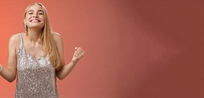 Sweet taste win. Charming happy blond girl rejoicing triumphing raise head up close eyes smiling broadly clench fists victory celebration gesture achieve dream come true, standing red background photo