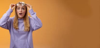 Shocked concerned young woman looking student ruin work staring disturbed upset take-off glasses popping eyes camera gasping speechless terrible acciddent happened, orange background photo