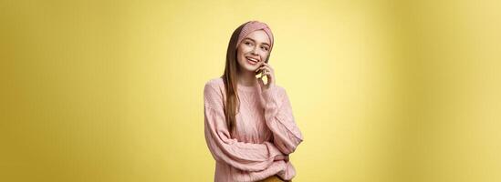 Talkative attractive glamour young 20s european woman wearing sweater, knitted headband tilting head looking away smiling curious, enjoying pleasant conversation via smartphone, talking to friend photo