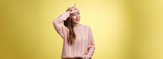 Attractive triumphing arrogant and confident cute glamourous woman in knitted sweater, headband showing l letter on forehead, loser sign and laughing over lost team, mocking having fun photo