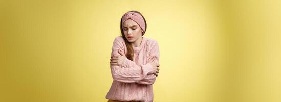 Brr girl freezing, turn-on heater. Portrait of timid cute woman wearing knitted sweater trembling from cold, embracing herself on arms looking down, stooping from discomfort cool temprature photo