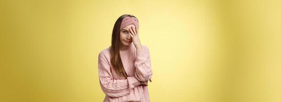 Woman facepalming covering face annoyed, bothered and inrritated, smirking looking with dismay, pissed off, posing unhappy displeased, staring indignant and upset posing tired over yellow background photo