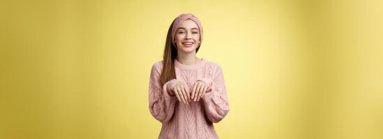 Girl pretends easter bunny. Charming cute female in knitted sweater holding palms like rabbit smiling happily, mimicking pretty animal fooling around from happiness and joy against yellow background photo