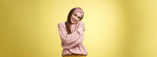 Girl feeling warm and safe thanks charming boyfriend embracing herself romantically hugging leaning on shoulder enjoying warmth of fluffy sweater, smiling tender in love over yellow background photo