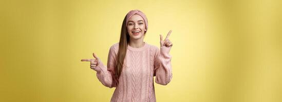 recoger qué desear. carismático alegre joven hembra estudiante en venda, suéter señalando arriba, indicando Derecha sonriente lindo, promoviendo anuncio demostración oportunidades y opciones terminado blanco pared foto