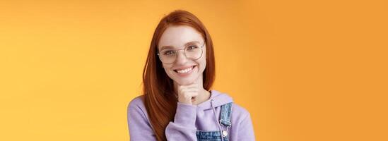 Creative outgoing young charismatic redhead female coworker discuss casual staff smiling laughing happily have pleasant conversation look camera amused tender touch chin, orange background photo