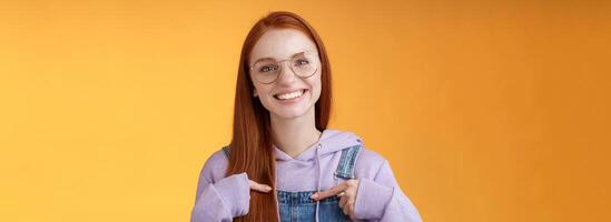 Happy lively friendly redhead european girl pointing herself suggesting help boasting telling own accomplishments smiling white teeth delighted volunteering, being picked, orange background photo