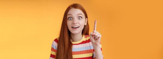 Great idea striked mind. Attractive excited surprised redhead woman open mouth smiling amused raise index finger eureka gesture stare camera shocked found solution have perfect plan photo