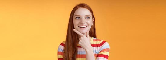 Creative satisfied smart redhead girl got excellent idea touching chin smiling broadly delighted good thought look upper left corner thinking pondering made up choice wanna implement plan photo