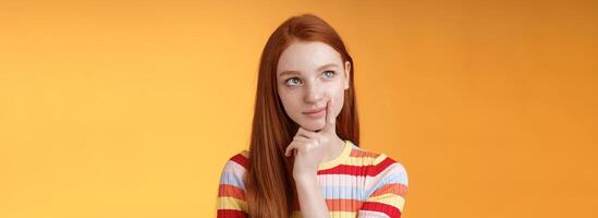 Creative thoughtful young smart redhead female student thinking ideas project look upper left corner dreamy touching lip pondering choice, taking important decision what order, orange background photo