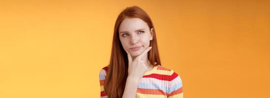 Hmm interesting. Suspicious doubtful attractive european redhead female pondering choice look hesitant thoughtful touch chin smirking tricky look upper left corner thinking, take decision photo