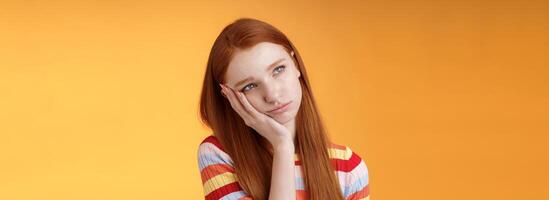 Lonely upset moody cute redhead girlfriend feeling boredom leaning palm look up pouting frowning displeased standing uneasy attend boring meeting, staring uninterested reluctant orange background photo