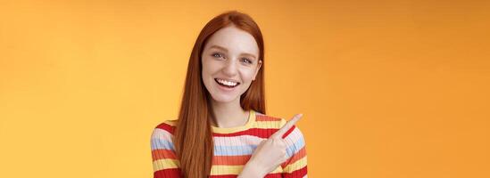 simpático saliente guapo jengibre niña Universidad estudiante que se discute conferencia compañera de clases sonriente riendo señalando Superior izquierda esquina cuestionado curioso saber detalles en pie naranja antecedentes foto