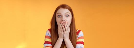 Excited shocked redhead speechless girl like gossiping standing emotional astonished hear amusing story gasping full disbelief cover mouth palm amazed posing orange background impressed photo