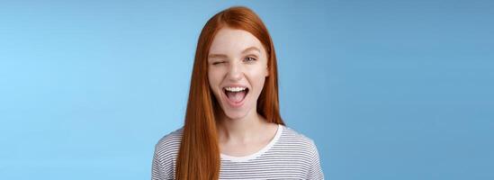 Cheeky good-looking flirty young gorgeous redhead girlfriend winking sassy smiling delighted open mouth hinting have interesting suggestion keep secret standing amused blue background photo