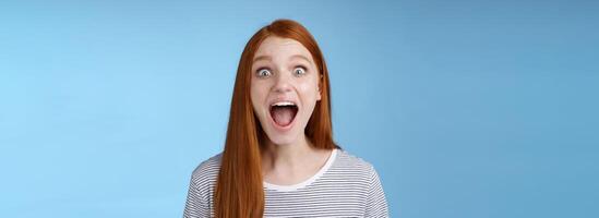 Amused thrilled enthusiastic surprised good-looking redhead girl wide eyes stunned drop jaw screaming astonished look impressed excited awesome news hearing incredible rumor, blue background photo