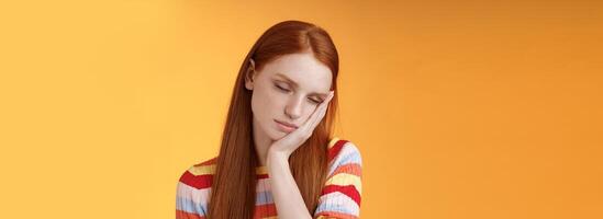 Tired cute redhead female student exhausted feel sleepy fall asleep standing leaning face palm close eyes working part-time night shift, daydreaming lacking energy wanna sleep bed orange background photo