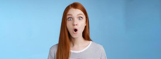 Wow omg fascinating. Impressed surprised amused good-looking redhead girl folding lips astonished wide eyes stunned reacting incredible cool promo standing blue background speechless photo