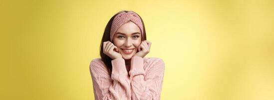 Waist-up shot of silly glamour timid girlfriend in knitted sweater shining from joy and positive emotions, holding hands on cheeks delighted and pleased blushing joyfully, standing amused photo