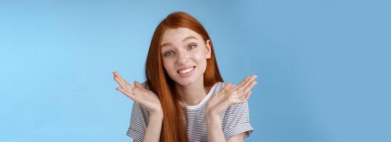 Awkward apologizing cute redhead girlfriend say sorry shrugging spread hands sideways puzzled smiling uncomfortably standing clueless unaware forgetting meeting, posing blue background photo