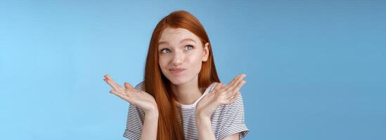 Awkward uncomfortable attractive redhead popular girl trying think up excuse feeling reluctant uncertain standing doubtful shrugging spread hands sideways smirking look up hesitant photo