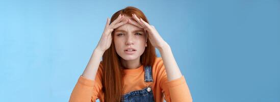 Puzzled unsure cute funny redhead european woman searching someone squinting cannot see without glasses peer into distance hold hands forehead cover sight sunlight, standing blue background photo