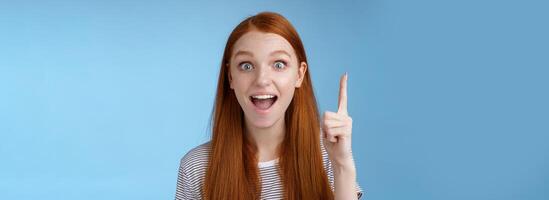 Excited good-looking cheerful ginger girlfriend add idea conversation raise index finger eureka gesture open mouth wide tell suggestion smiling broadly pondering excellent variant, blue background photo