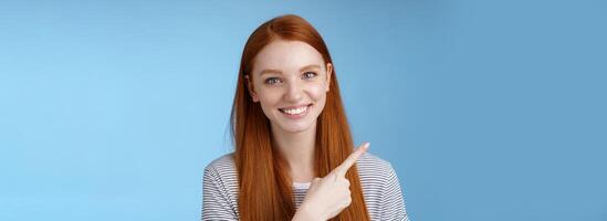 Close-up attractive gentle tender friendly-looking smiling redhead woman show place pointing upper left corner index finger grinning helpful giving choice help find store, standing blue background photo