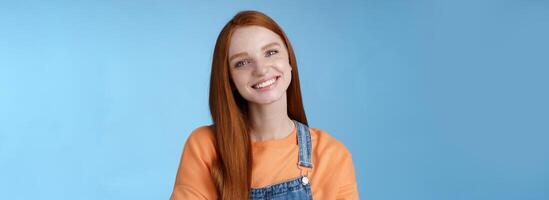 Charismatic kind pleasant redhead girl blue eyes smiling friendly listen politely customer standing blue background tilting head amused grinning cross hands chest professional confidence pose photo