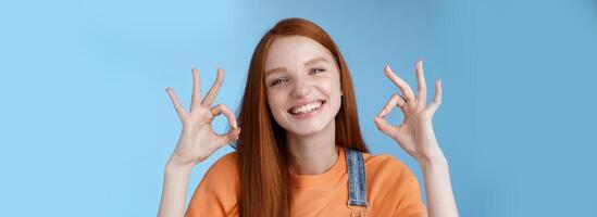 Wellbeing, happiness, perfection concept. Attractive friendly smiling joyful redhead female student show excellent okay ok gestures grinning approval agree awesome concept, satisfied blue background photo