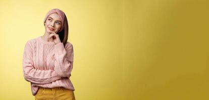 Dreamy attractive and stylish schoolgirl in knitted warm sweater, headband, thinking as smiling satisfied and devious having idea, looking at upper left corner thoughtful, daydreaming, planning photo