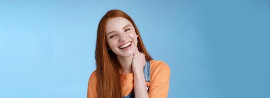 Carefree silly flirty young redhead girlfriend having fun enjoying lovely date summer evening laughing out loud smiling broadly tilting head touching neck shy blushing acting cute blue background photo