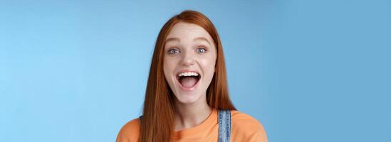 divertido carismático animado saliente jengibre niña emocionado teniendo divertido amigos Gritando decir un demostración Perfecto blanco sonrisa disfrutar simpático alegre atmósfera en pie emocionado positivo azul antecedentes foto