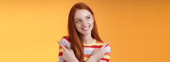 Dreamy cute redhead girl planning were go summer holidays have different choices picking variant look intrigued smiling pleased pointing sideways left right taking decision, orange background photo