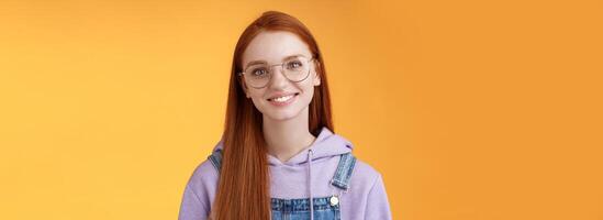 Charming smart cute female freelancer order coffee working cafe standing overalls glasses hoodie smiling delighted talking casually barista orange background have happy relaxing day feel joyful photo