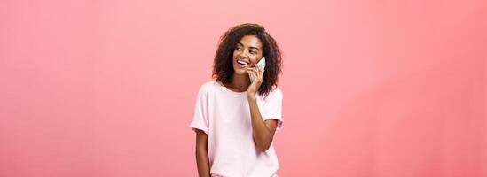 mujer vocación novio ven recoger su arriba después práctica en pie en calle despreocupado y frío mirando Derecha con ancho satisfecho sonrisa participación teléfono inteligente cerca oído posando terminado rosado antecedentes foto