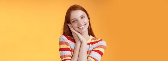 Lovely young flirty redhead european girl smiling broadly excited happy lean palm receive sweet tender present look grateful amused joyfully reacting pleasing moment, standing orange background photo